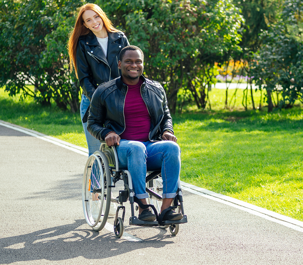 Woman pushing man in a wheelchair on a sidewalk